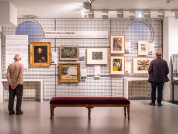 Besuchende vor der KUNSTWAND, einer Gitterwand, an der Thematisch zusammenpassende Werke aus der Sammlung des Lindenau-Museums hängen