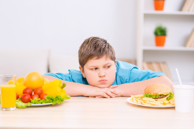 Dickeres Kind sitzt vor Essen: Salat oder Burger? Foto von yacobchuk von istock